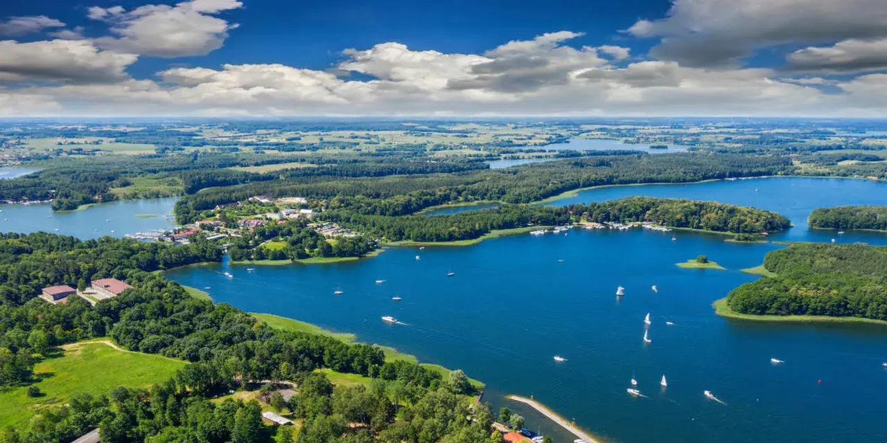 Malownicze, klimatyczne miejsca nad jeziorem, gdzie lasy schodzą do wody, a żaglówki unoszą się na błękitnej tafli.