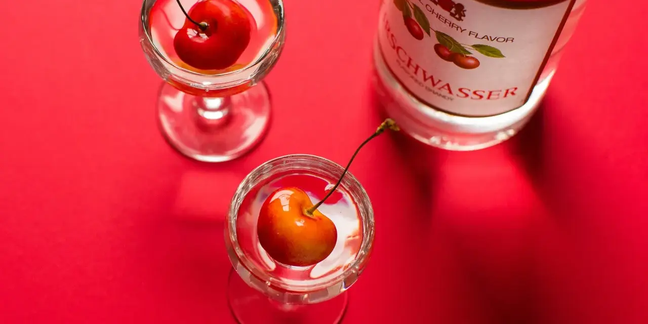 Zwei Gläser mit Kirschen und eine Flasche Kirschwasser auf rotem Hintergrund. Was ist Cherry? Ein süßer Genuss.