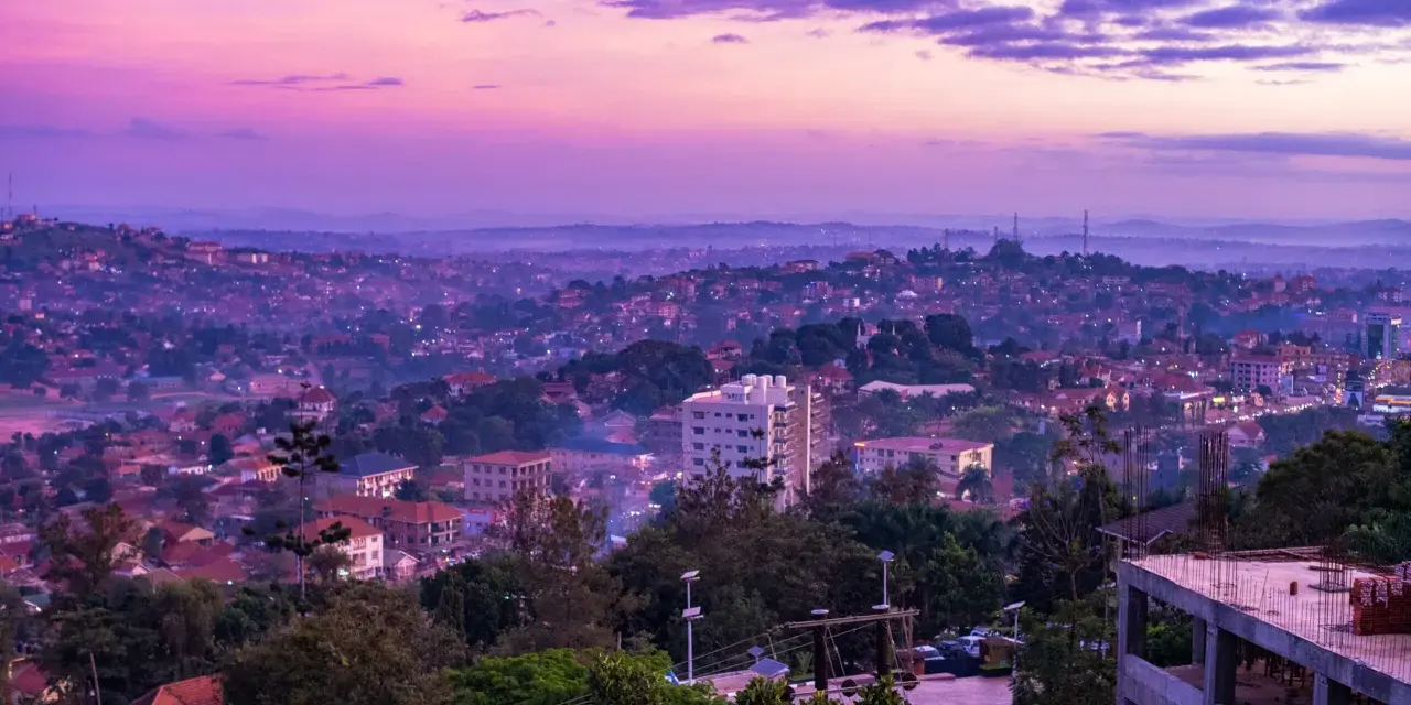Fioletowe niebo nad krajem z kampalą, z widokiem na wzgórza pokryte zabudowaniami i zielenią.