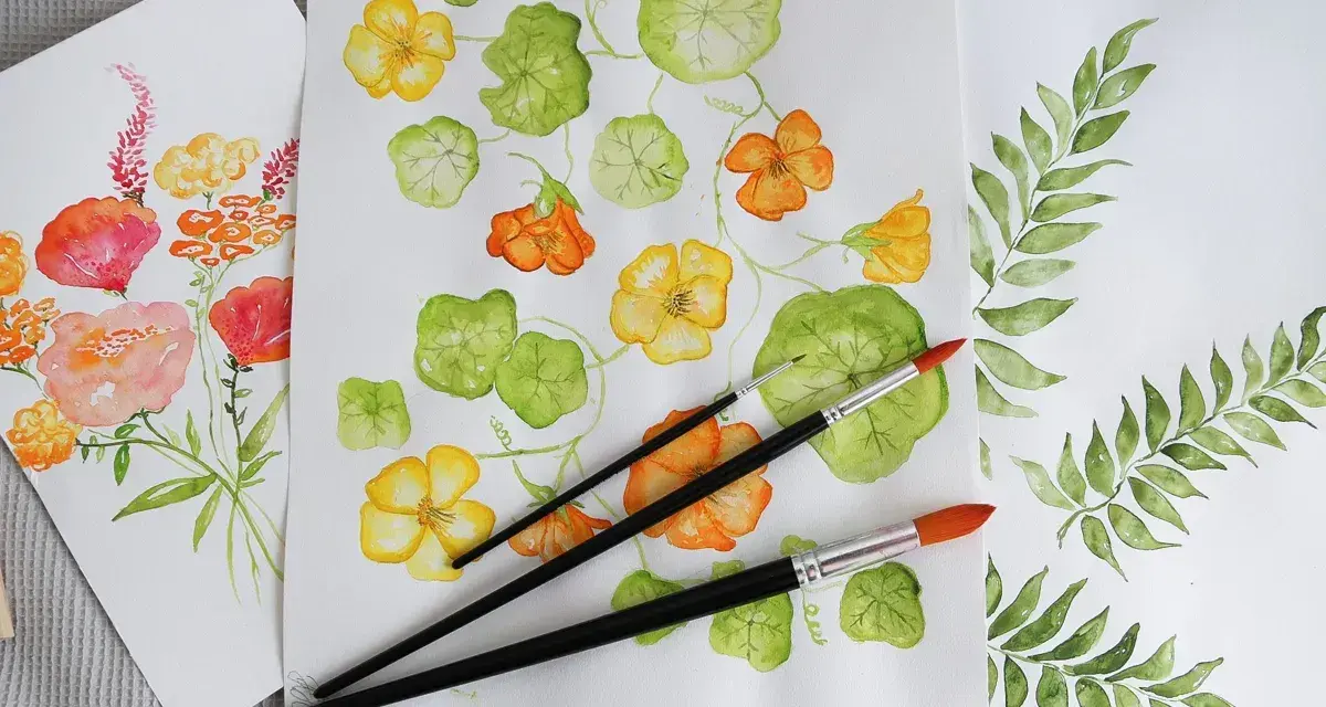 Flera akvarellmålningar med blommor och blad. En målning visar gula och orange blommor med gröna blad, en annan visar en bukett med rosa och orange blommor. Penslar ligger på pappret.