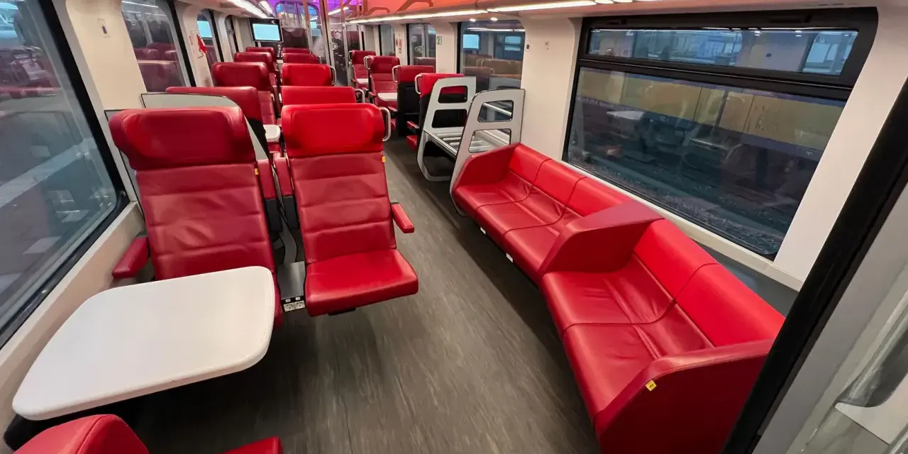 Interior of a modern train, with red leather seats and tables, ready for a journey from AMS to Brussels.