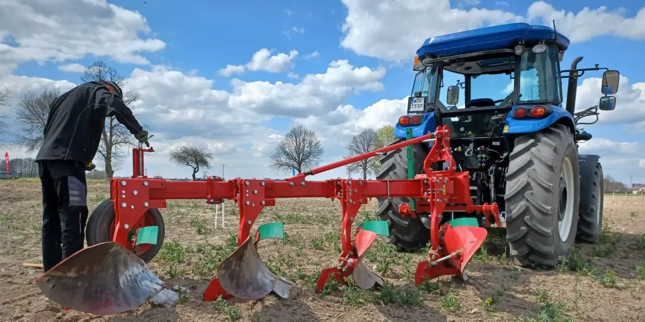 Rolnik przygotowuje pług do orania ziemi. Błękitne niebo z chmurami nad polem.