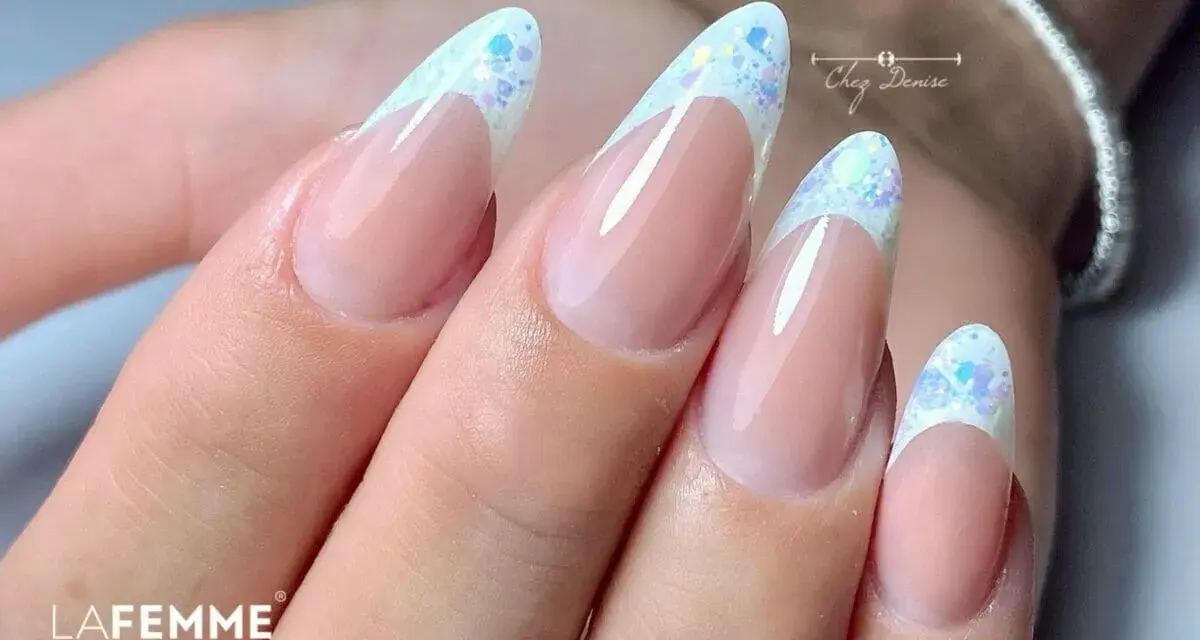 Unghie a mandorla con french manicure rivisitato: base nude e punta bianca con brillantini scintillanti, un tocco di french rosso con brillantini.