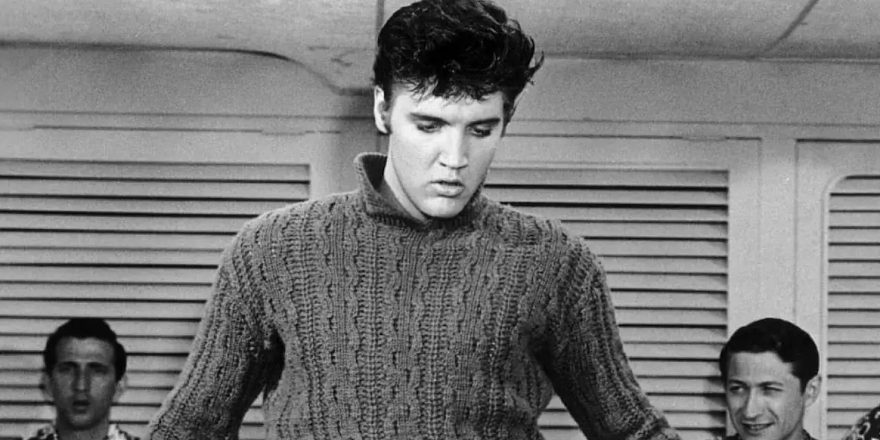 Elvis Presley in einem Strickpullover, vielleicht bei der Aufnahme seines letzten Liedes. Im Hintergrund zwei Männer.
