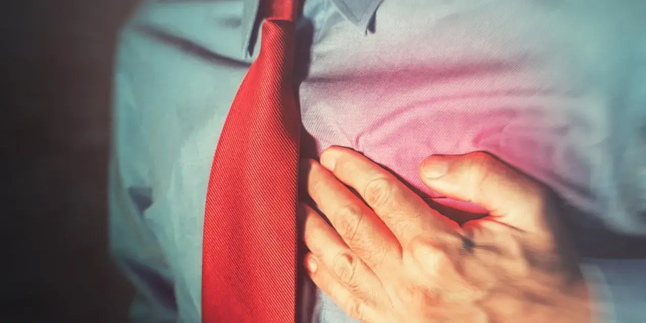 Mężczyzna w czerwonym krawacie trzyma się za serce, odczuwając ból. Może to być sygnał, by zadbać o swoje concor cor.