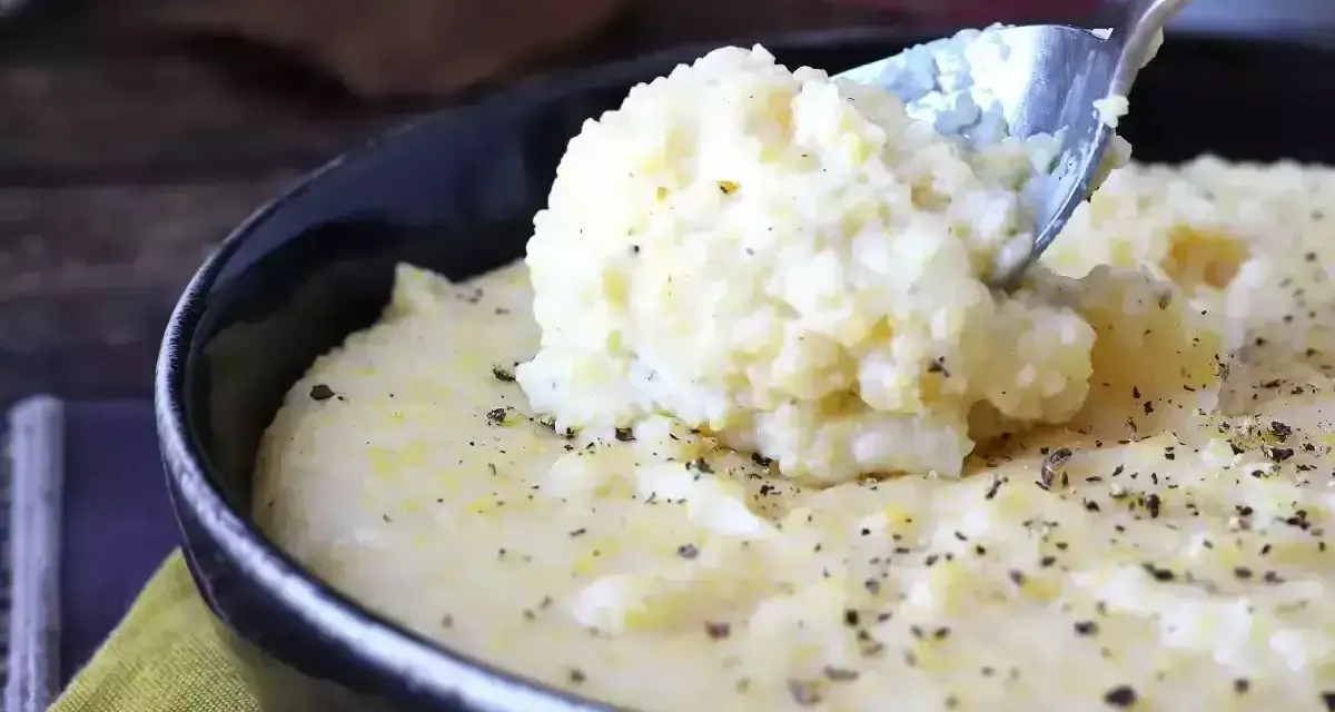 Kremowa polenta, idealna do prostego polenta przepis, posypana świeżo mielonym pieprzem, nabierana łyżką z czarnej miski.