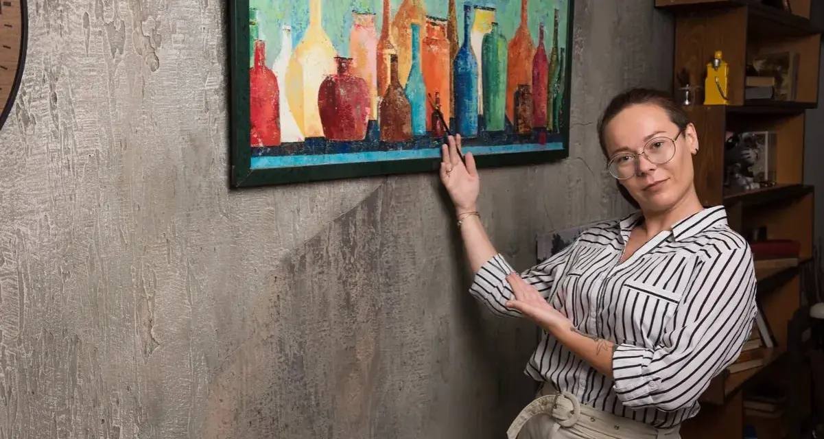 Une femme explique comment vernir un tableau, montrant une œuvre colorée de bouteilles.