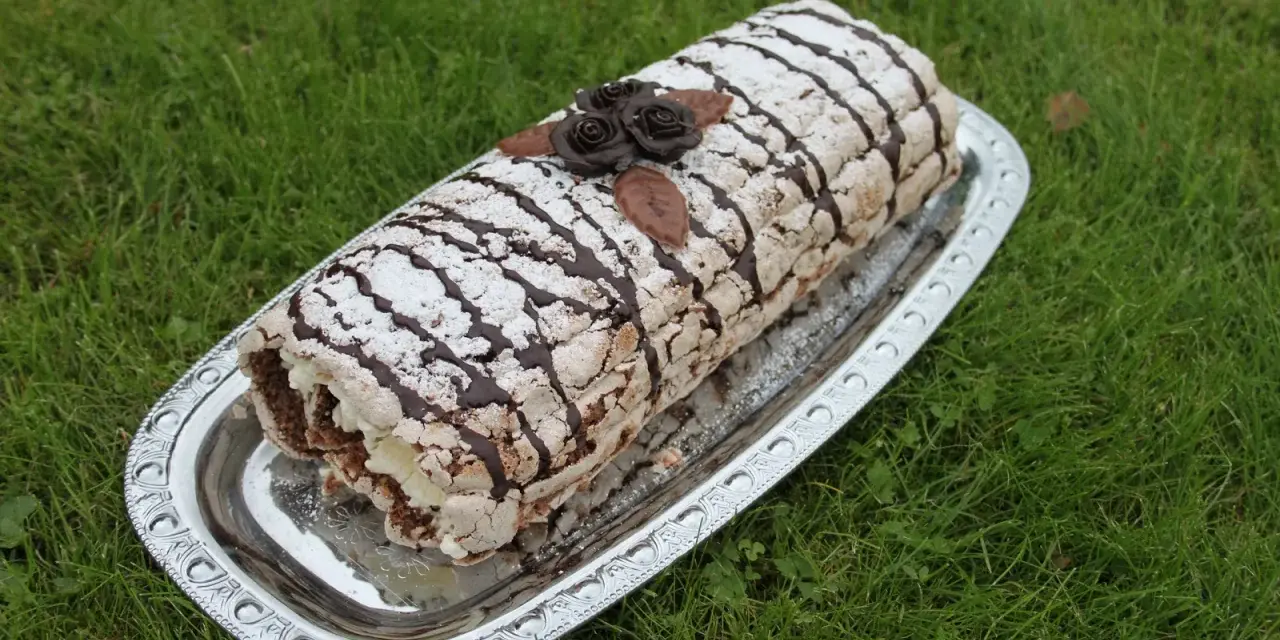 En läcker budapestrulle recept på ett silverfat, dekorerad med chokladrosor och pudersocker, på en grön gräsmatta.