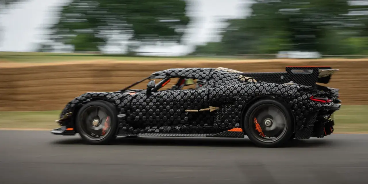 Czarny, pikselowy hypercar z pomarańczowymi akcentami pędzi po torze, tworząc wrażenie ruchu.