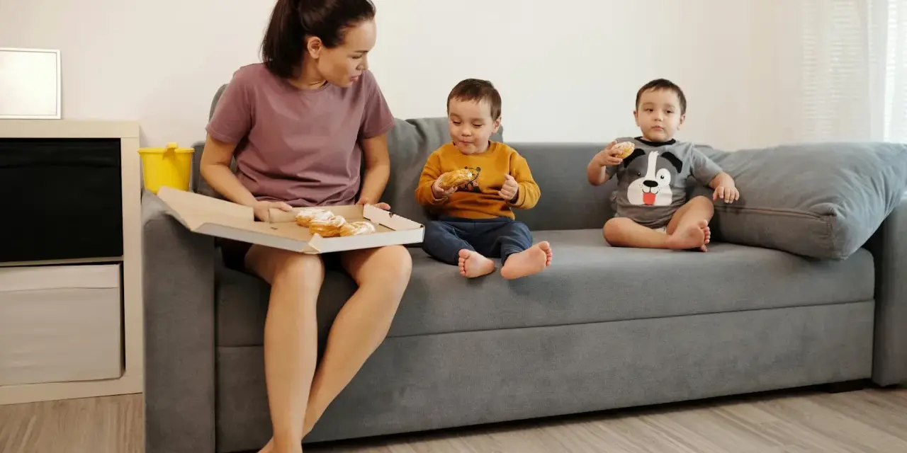 Mama z dziećmi na kanapie, choć jest zakaz słodyczy, wszyscy jedzą pączki.