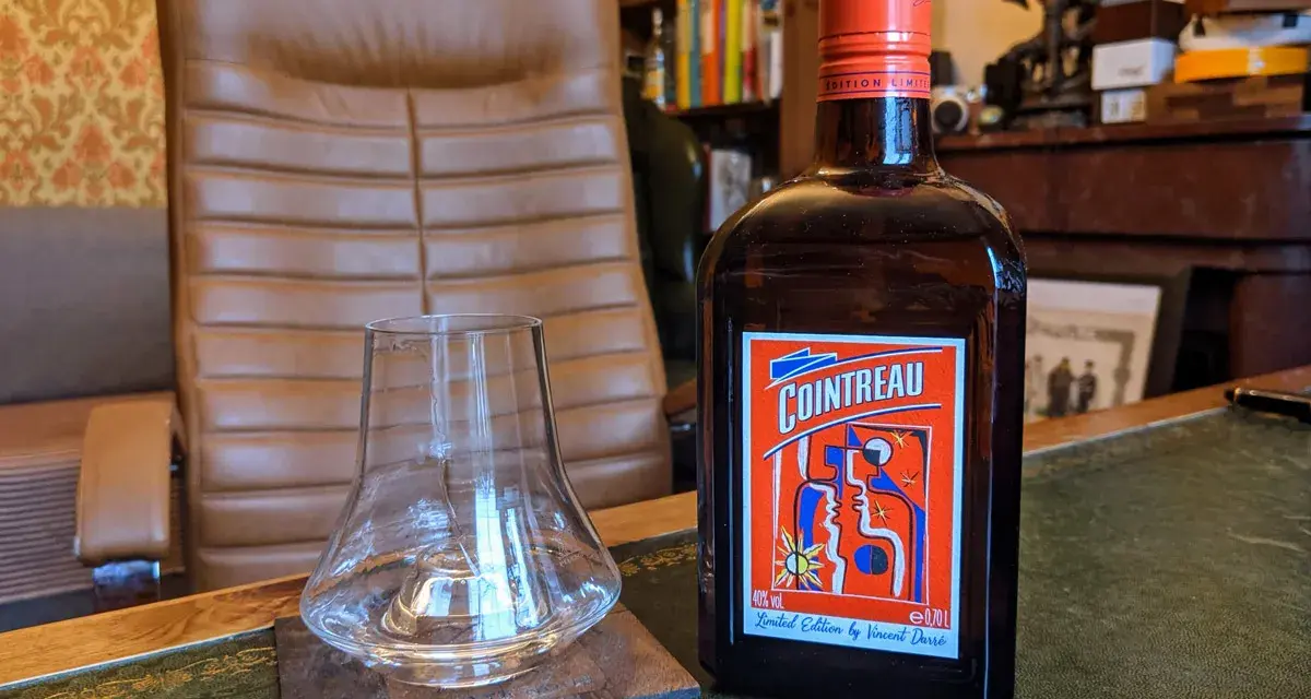 Cointreau kontra Triple Sec w koktajlach: butelka Cointreau i pusty kieliszek na biurku.