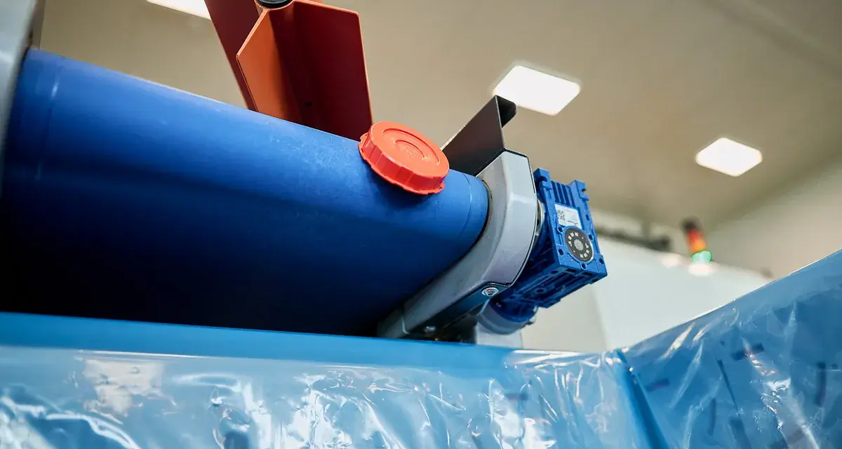 Maszyna do produkcji folii, z niebieskim wałkiem i pomarańczową nakrętką, przygotowuje materiał cerplast do dalszej obróbki.