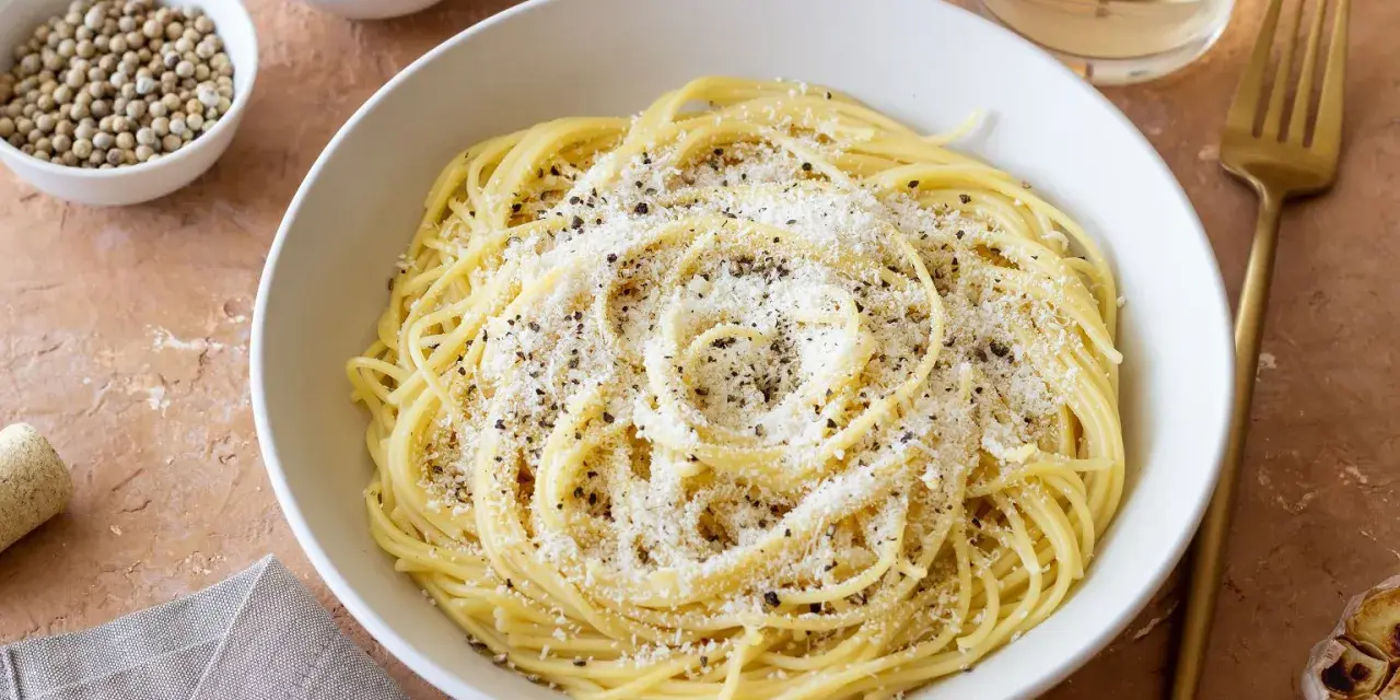 Miseczka spaghetti posypana parmezanem i pieprzem, obok przyprawy i czosnek.
