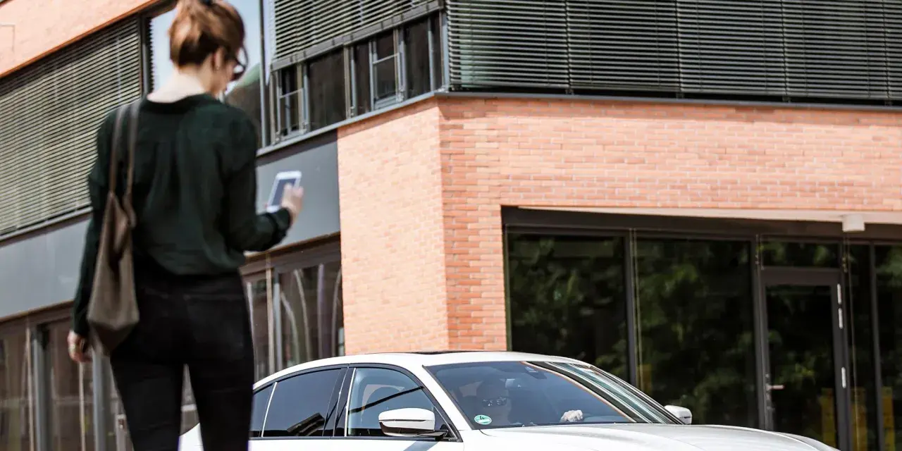 Frau mit Smartphone wartet auf FREE NOW Fahrt. Keine Beschwerde, nur Vorfreude auf die Fahrt.