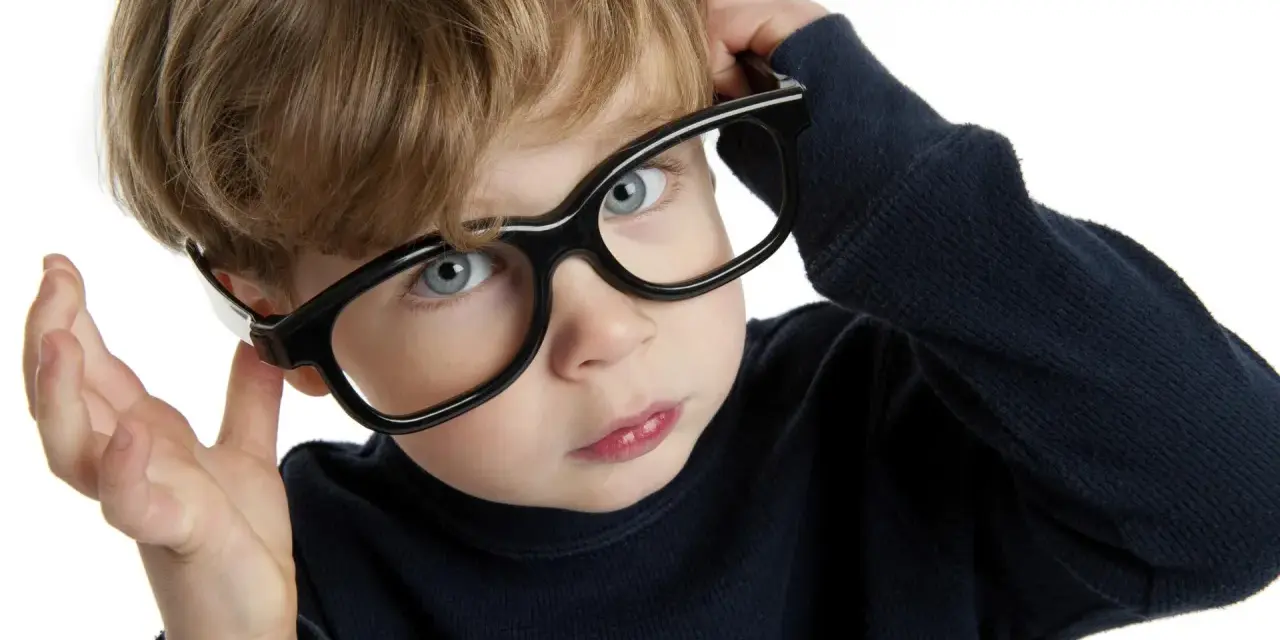Chłopiec z niebieskimi oczami poprawia okulary, zastanawiając się nad nadwzrocznością u dzieci kiedy okulary są potrzebne.