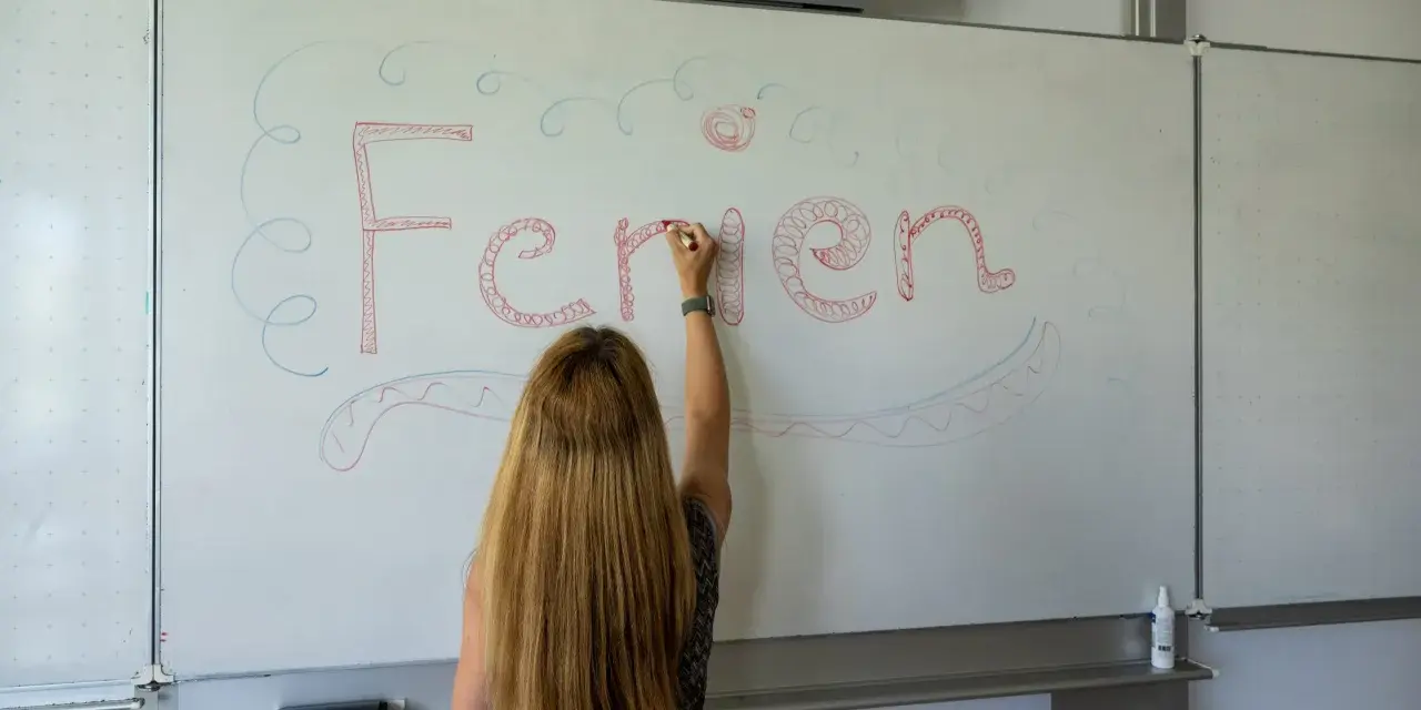 Frau schreibt "Ferien" an Tafel, Vorfreude auf Pfingstferien Rheinland-Pfalz.