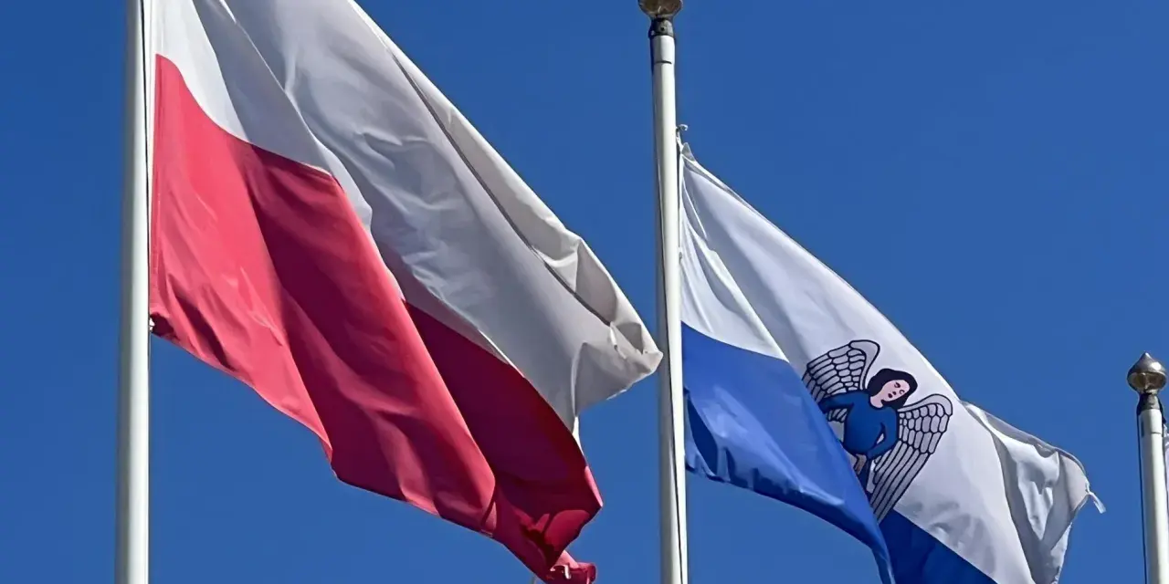 Flaga Torunia i biało-czerwona flaga Polski powiewają na tle błękitnego nieba.