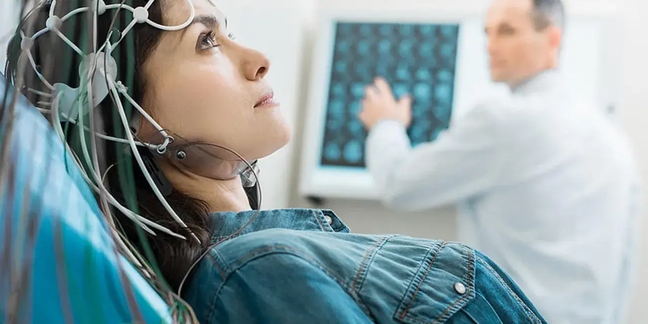 Frau mit EEG-Kappe für eeg medizinische Untersuchung, Arzt deutet auf Bildschirm mit Gehirnscans.