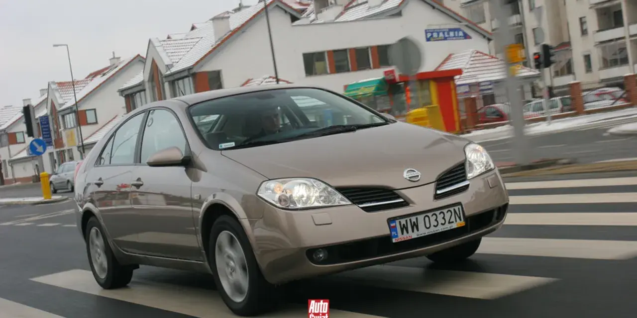 Brązowy Nissan Primera przejeżdża przez pasy na tle zaśnieżonych domów.