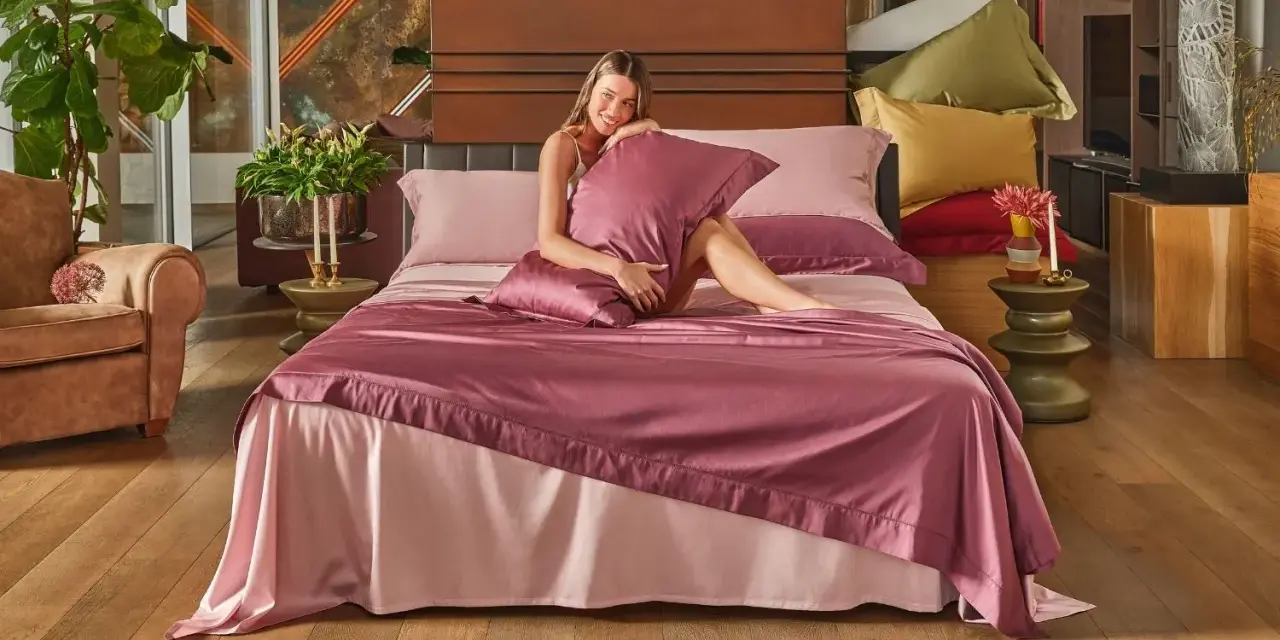 Una donna sorride su un letto con lenzuola rosa. Per mantenerle fresche, si lavano a 40 gradi.