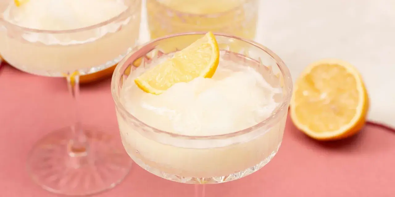 Erfrischendes Limoncello Sorbet in einem Kristallglas, garniert mit einer Zitronenspalte. Ein halbe Zitrone liegt daneben.