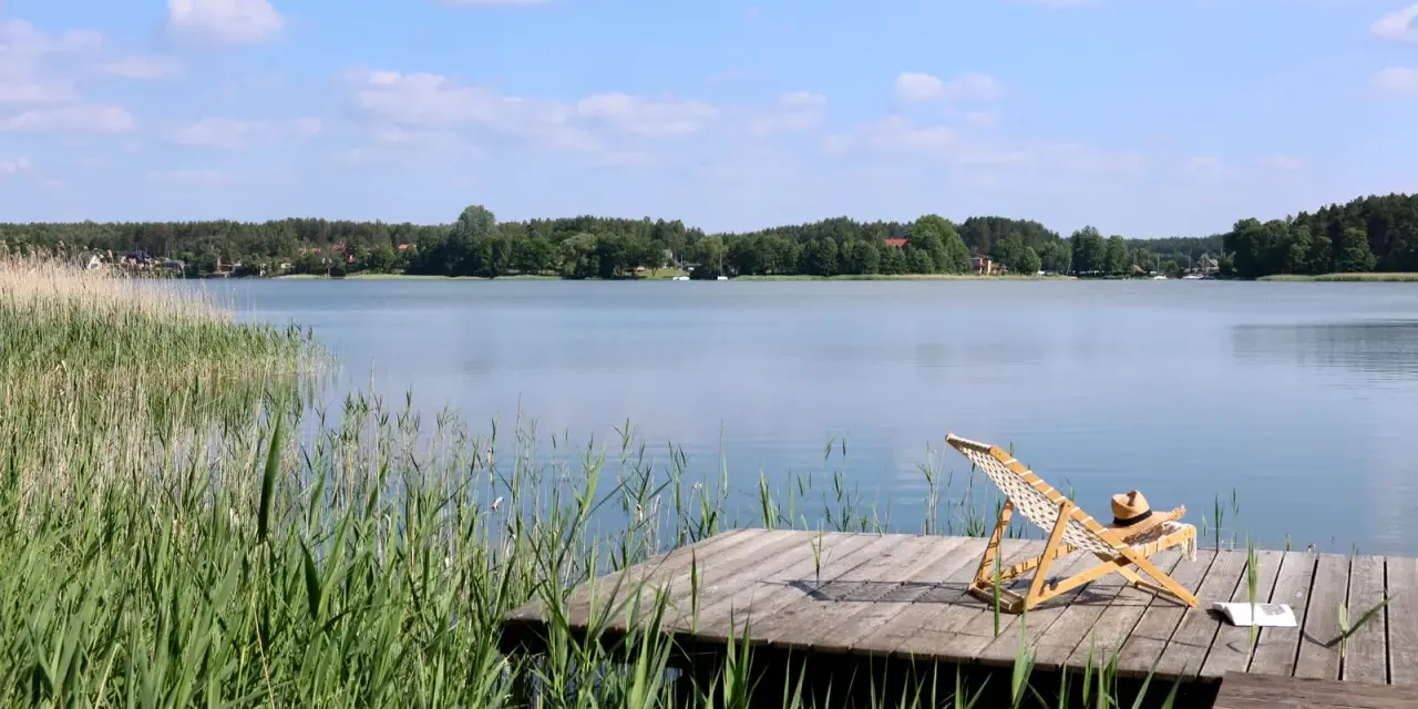 Spokojne kaszubskie jeziora, drewniany pomost z leżakiem i książką, otoczone trzcinami i lasem.