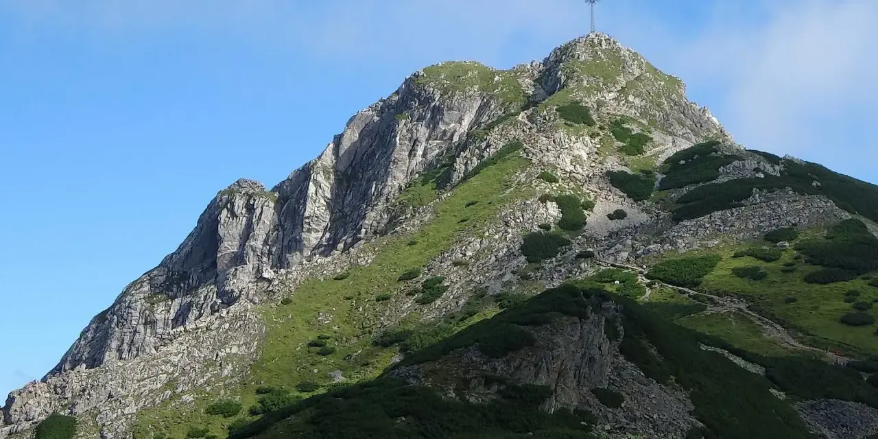 Szczyt Giewontu z krzyżem, zielone zbocza, kamienie i ścieżka. Wjazd na Giewont jest darmowy, ale wymaga wysiłku.