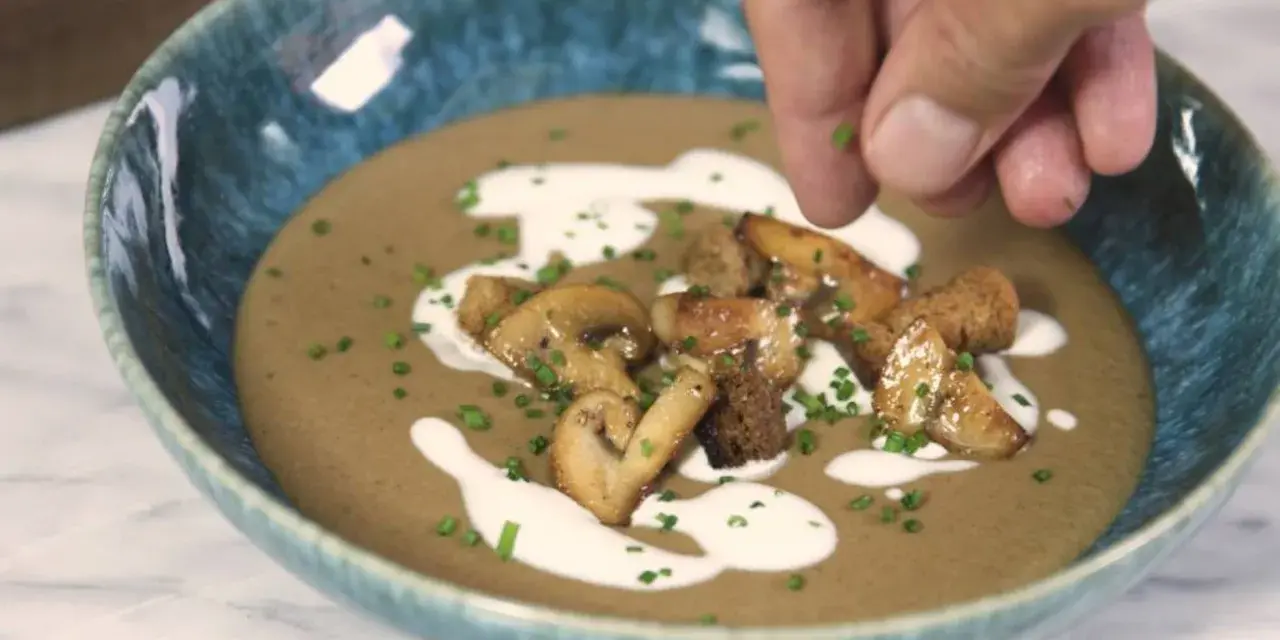 Crema de champiñones servida en un cuenco azul, decorada con champiñones salteados, picatostes y un chorrito de nata.