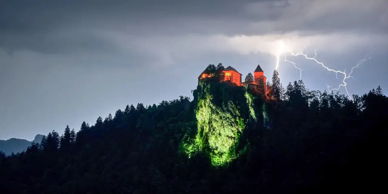 Zamek Poenari, oświetlony na czerwono, góruje nad skalistym zboczem podczas burzy z piorunami.