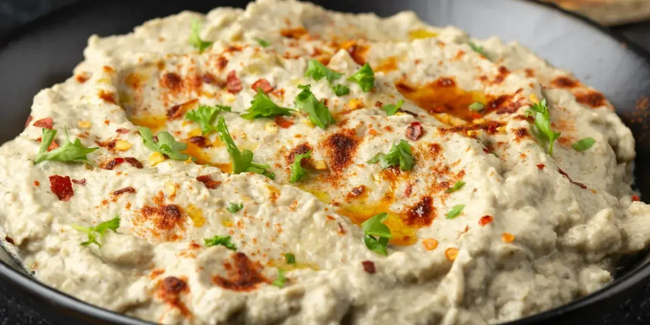 Kremowa pasta z bakłażana, doprawiona papryką i posypana natką pietruszki, w czarnej misce. Idealna do pieczywa.