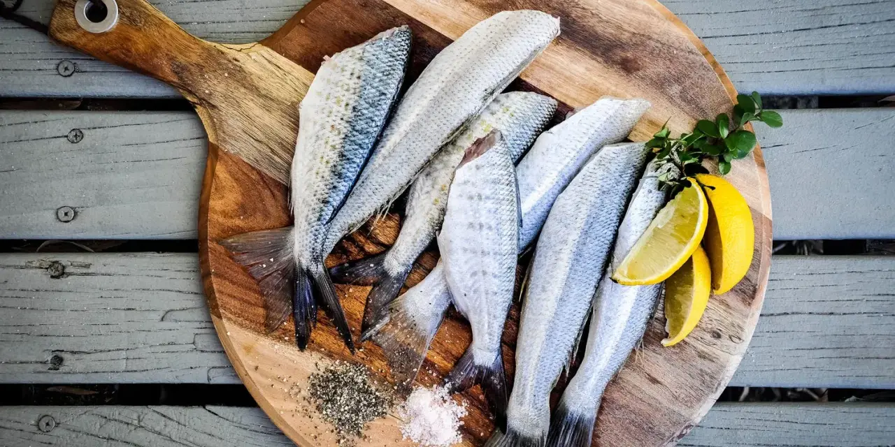 Plusieurs poissons frais sur une planche à découper en bois avec du sel, du poivre et des quartiers de citron.