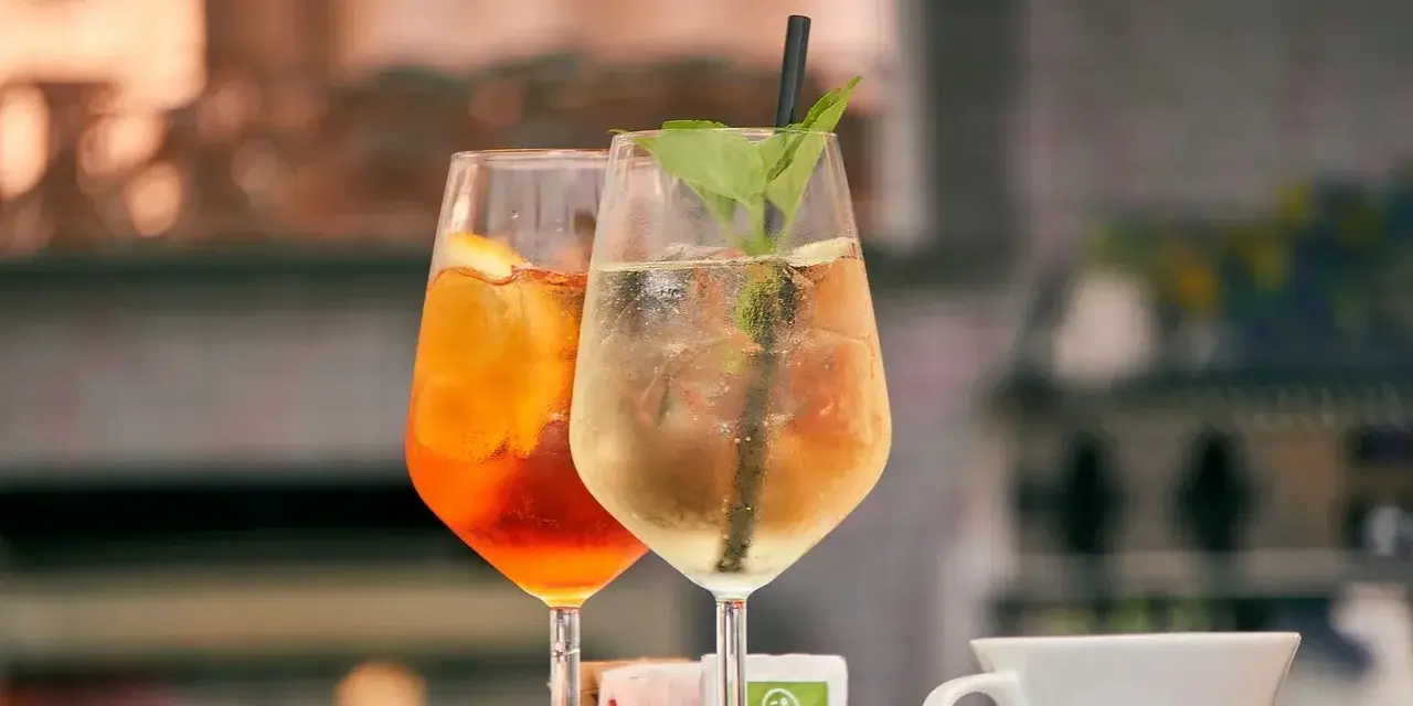 Dwa drinki w kieliszkach: pomarańczowy Aperol i jasny, z miętą. Aperol kontra Campari – wybór należy do Ciebie!