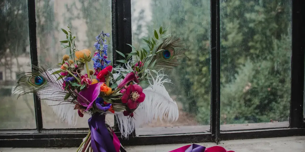 Bogaty bukiet z pawimi piórami i fioletowymi wstążkami. Każdy kwiat ma swoje znaczenie, tworząc kompozycję pełną symboliki.
