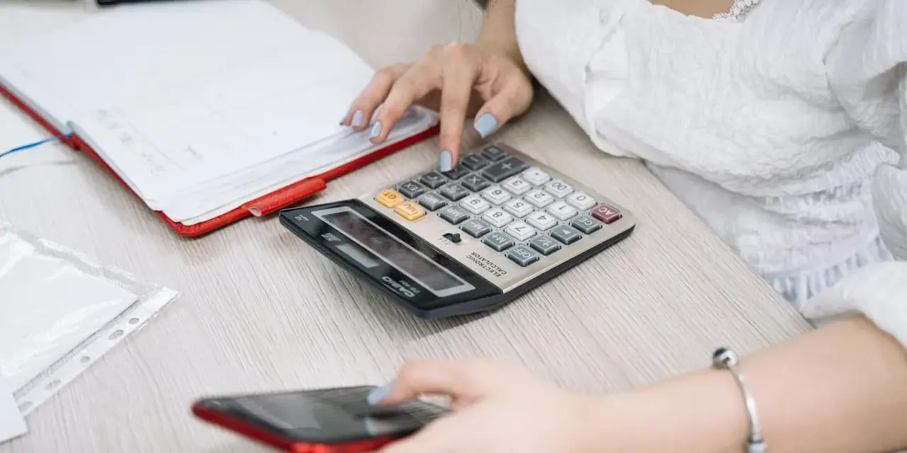 Kobieta liczy na kalkulatorze, przygotowując się do rozliczenia podatkowego w Holandii. Obok leży telefon i notatnik.