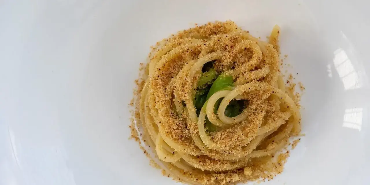 Spaghetti conditi con aglio, olio e peperoncino, cosparsi di pangrattato croccante e qualche foglia verde.