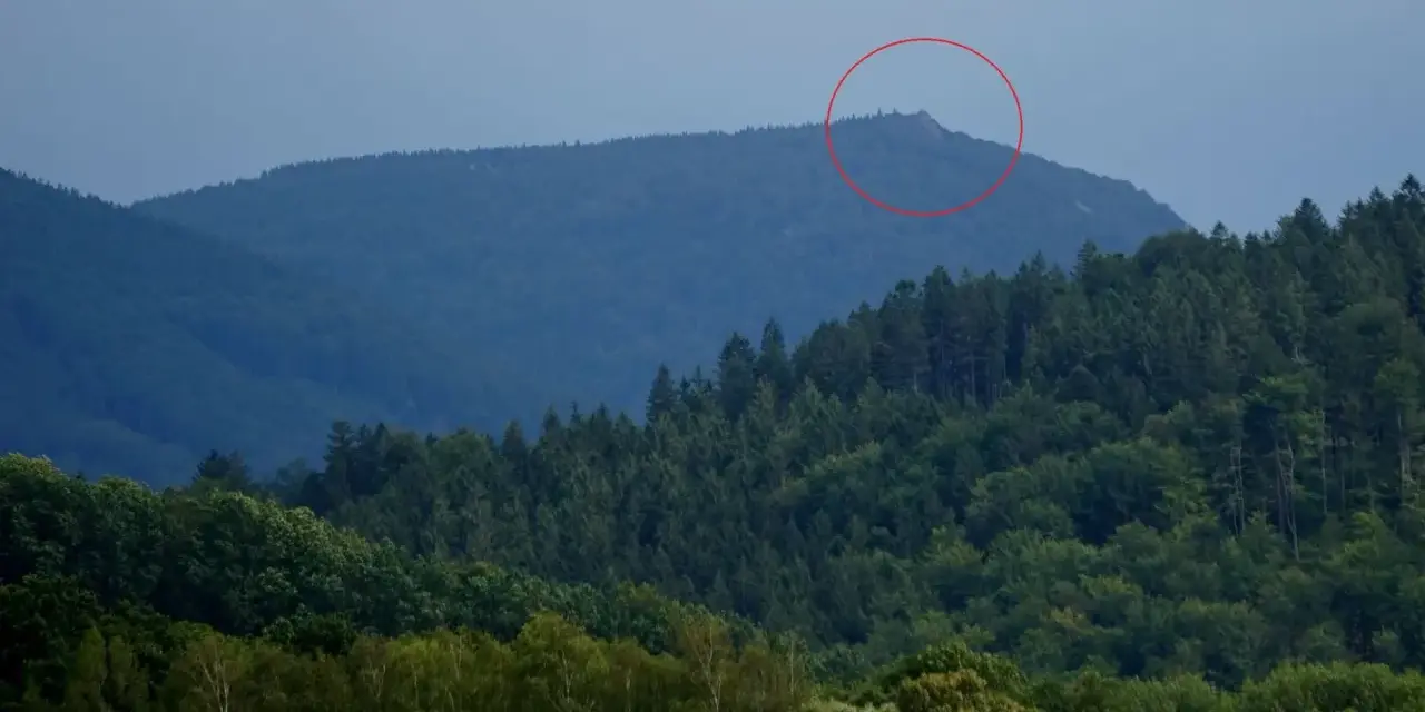Górzyste krajobrazy czeskich Izery, z zalesionymi zboczami i skalistym szczytem zaznaczonym czerwoną obwódką.