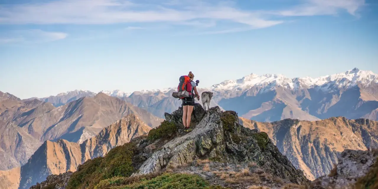 Escursionista con cane su cresta rocciosa, sfondo di montagne innevate nei GR10 Pirenei.