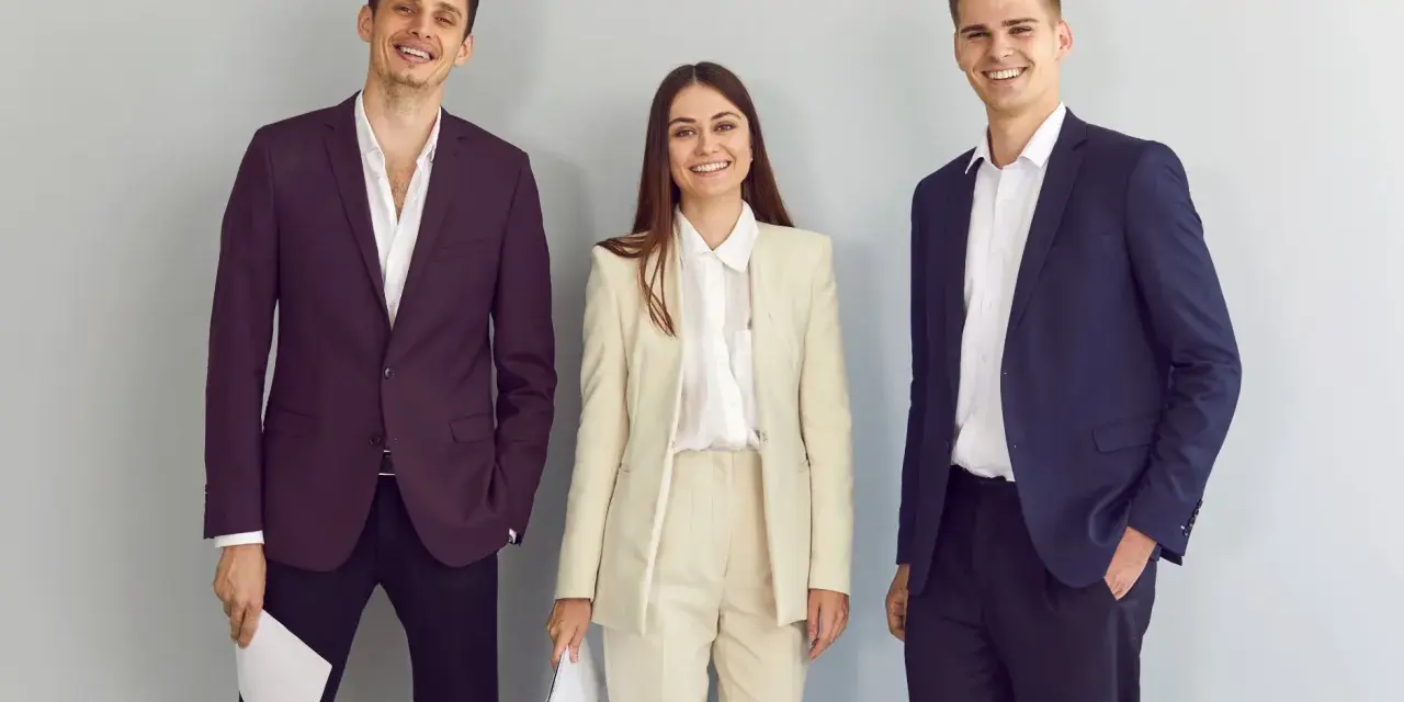 Trzy uśmiechnięte osoby w eleganckich strojach, idealnych na rozmowę o pracę. Dowiedz się, jak się ubrać na rozmowę o pracę!
