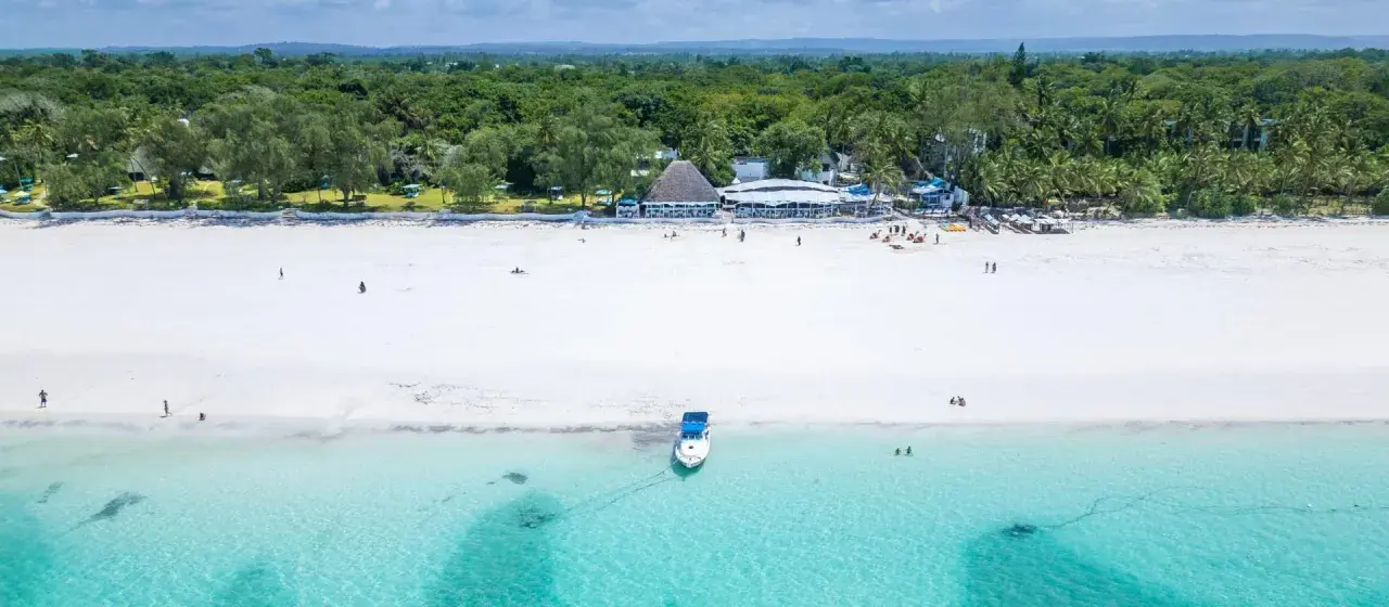Idealne kenia wakacje: biała plaża, turkusowa woda, łódź i tropikalna roślinność.