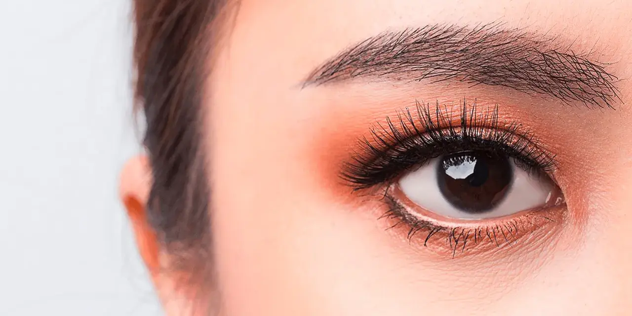Occhi luminosi con un tocco di trucco coreano: ombretto pesca, eyeliner sottile e ciglia lunghe e folte.