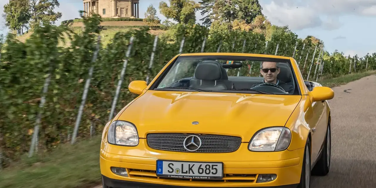 Gelber Mercedes SLK R170 Cabrio fährt durch Weinberge, im Hintergrund ein Tempel.