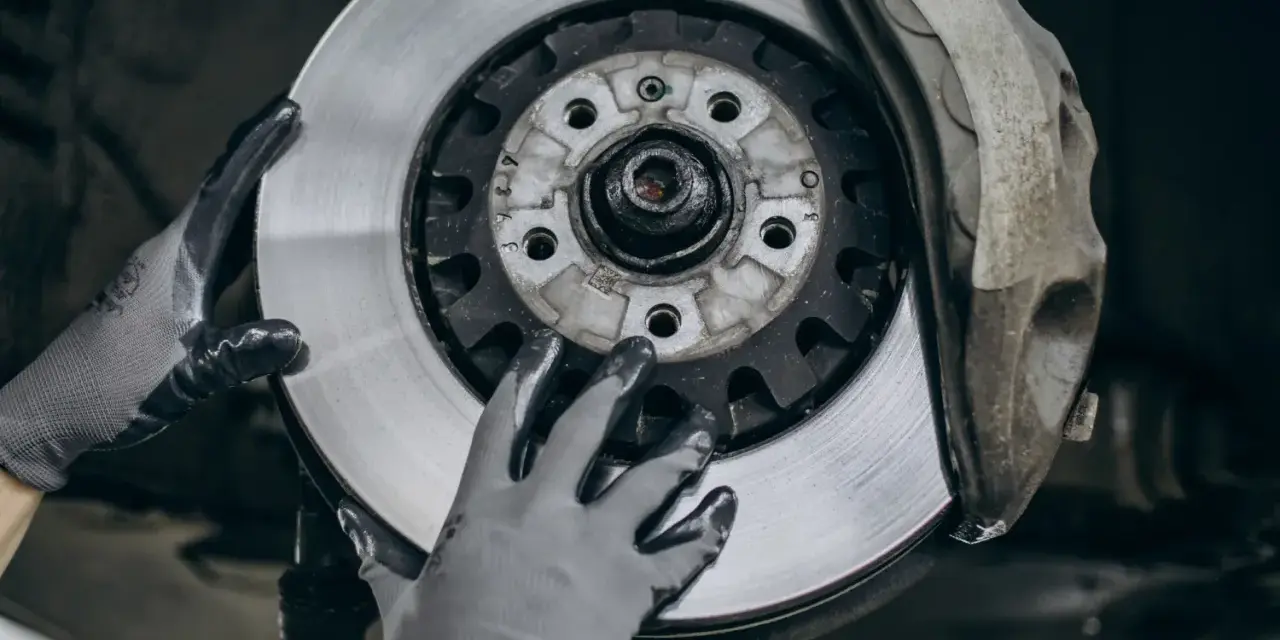 Mechanik w rękawiczkach wymienia zużyte tarcze hamulcowe. Widać nowy, lśniący element obok starego zacisku.