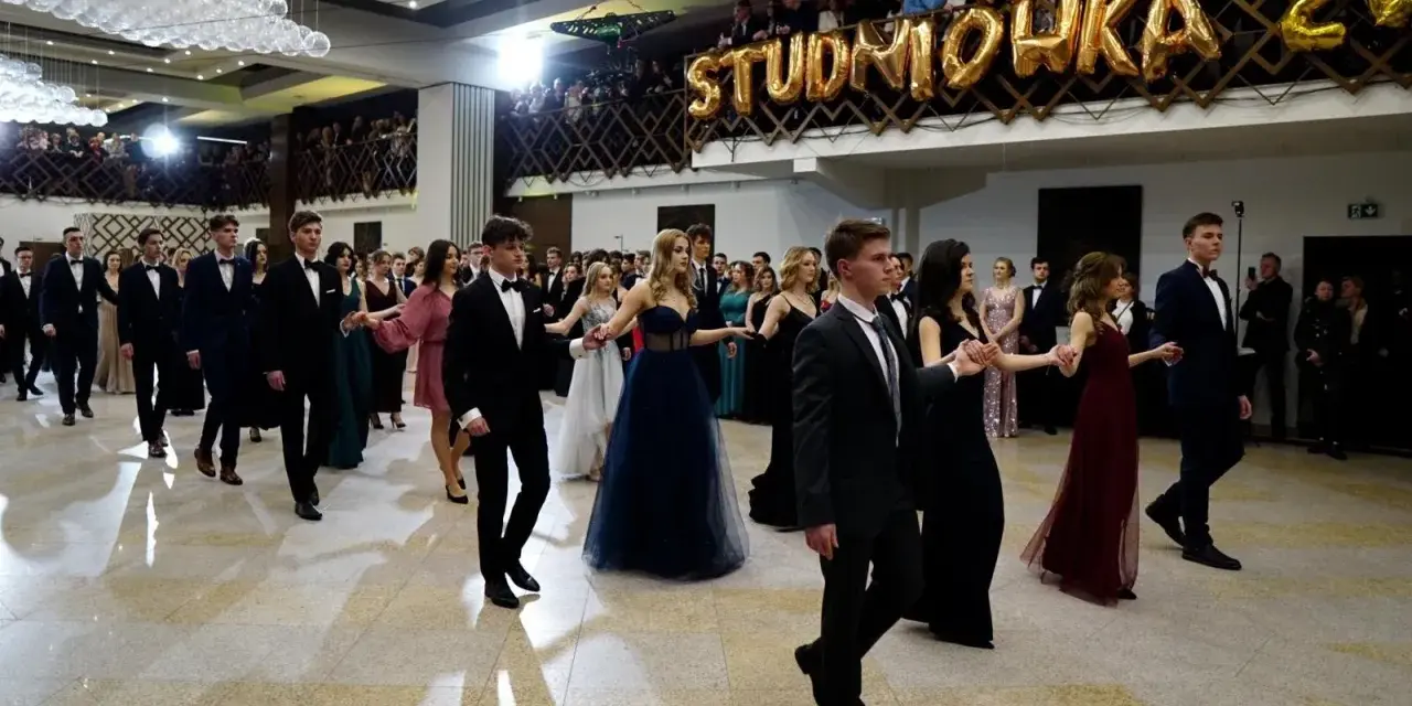 Młodzi ludzie w eleganckich strojach, tańczący poloneza na balu studniówkowym.