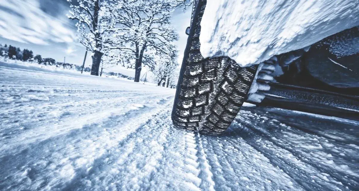 La gomma ghiaccio affronta la neve su una strada invernale, lasciando profonde tracce. Alberi innevati sullo sfondo.