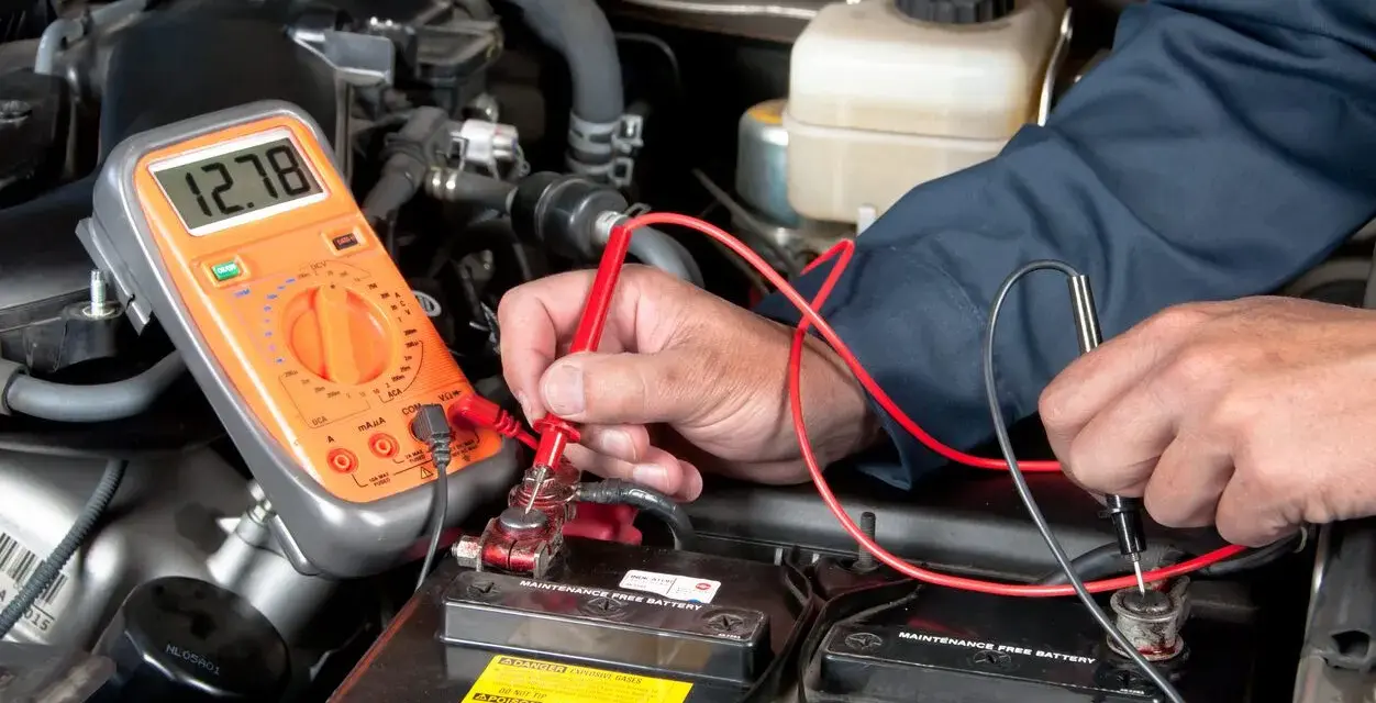 A person uses a multimeter to test a car battery in an engine bay.