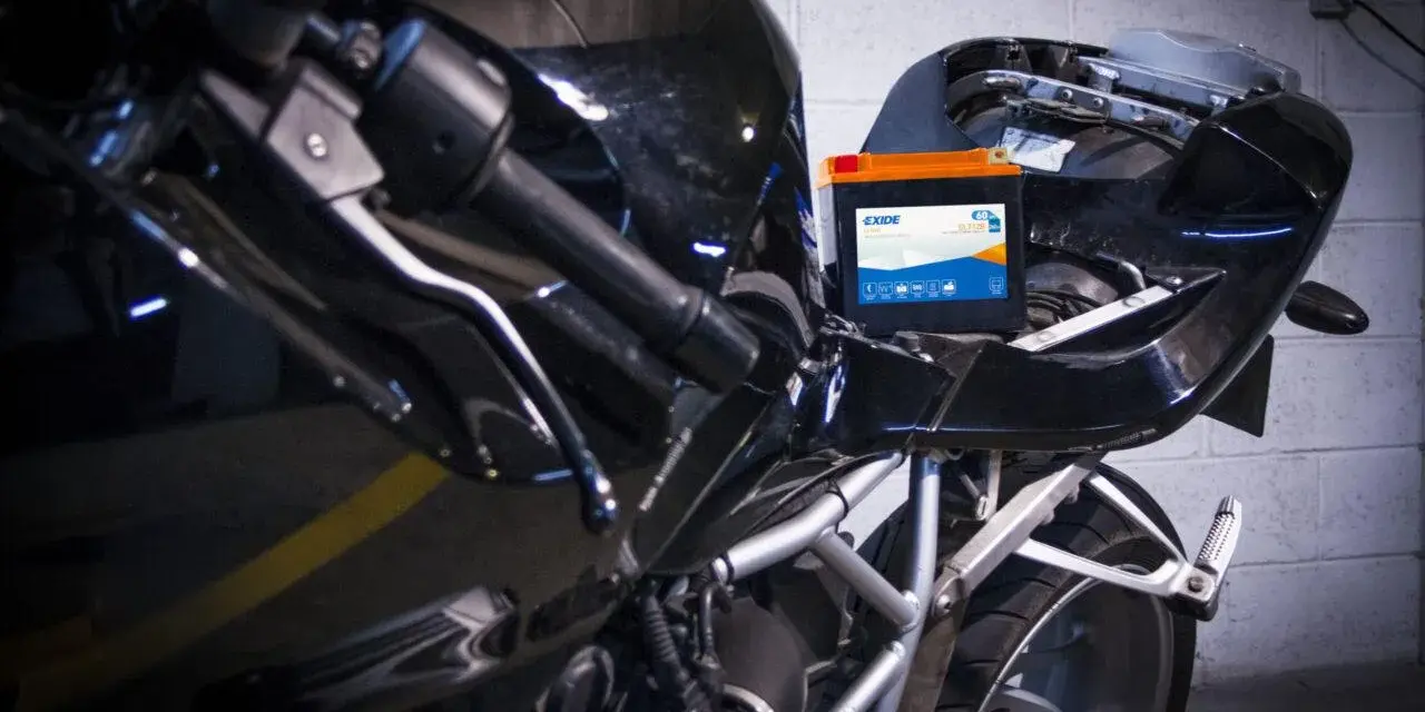 Una batteria nuova va caricata. La nuova batteria Exide è posizionata sul telaio di una moto nera lucida, pronta per essere collegata.