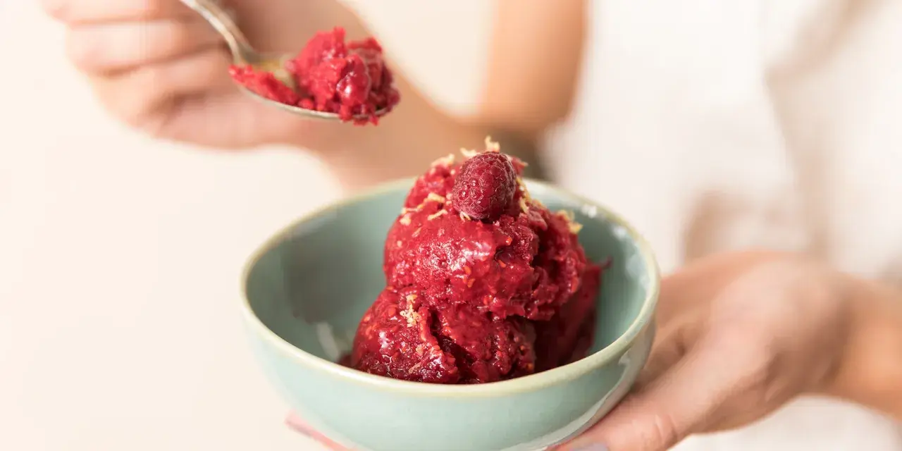 Ein Löffel Himbeersorbet-Rezept wird über eine Schüssel mit dem leuchtend roten Dessert gehalten, garniert mit einer Himbeere.