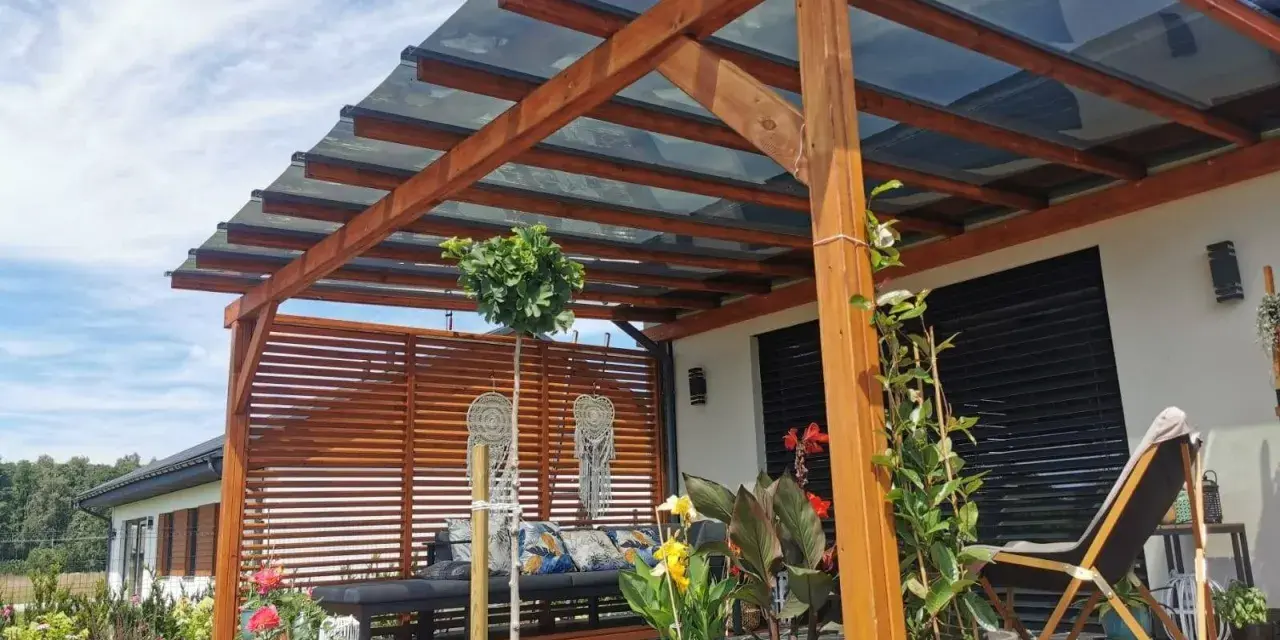 Drewniana pergola z przezroczystym dachem to idealne rozwiązanie co na dach tarasu. Wygodny wypoczynek wśród roślin i kwiatów.