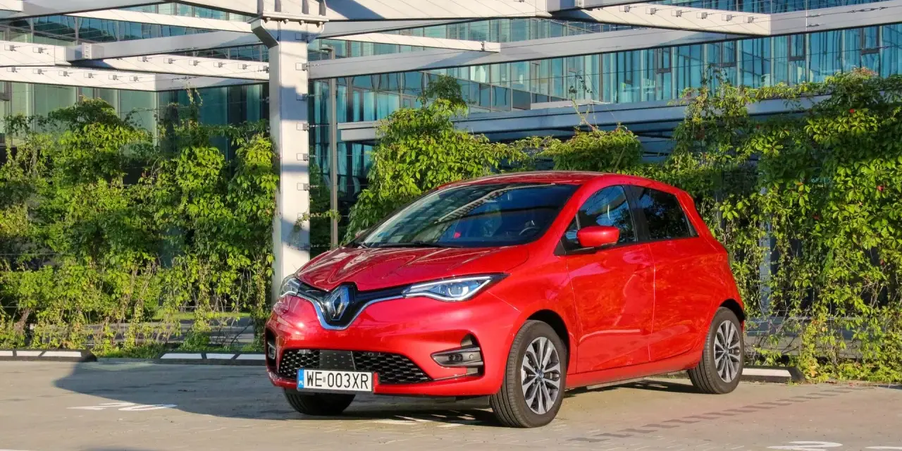 Czerwony Renault Zoe, elektryczny samochód miejski, gotowy do jazdy. Jego imponujący zasięg pozwala na swobodne podróżowanie po mieście i poza nim.