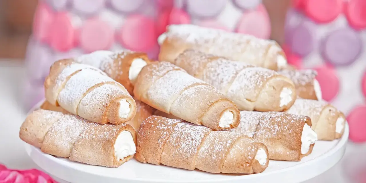 Domowe rurki z kremem, posypane cukrem pudrem, wyglądają apetycznie obok pastelowych dekoracji.